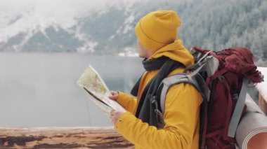 Dağlarda seyahat. Genç uzun yürüyüşe çıkan kimse bir kağıt harita alanı kullanır. Yolunu arar. Macera ve seyahat hoşlanıyor. Bir arka plan kış dağlar ve güzel bir göl üzerinde