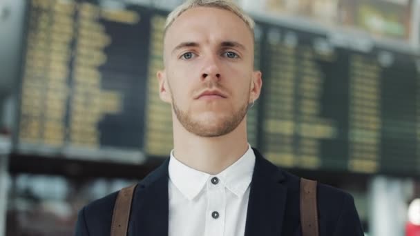 Portret van jonge aantrekkelijke zakenman in de camera op de luchthaven op vertrek planken achtergrond kijkt, voelt gelukkig — Stockvideo