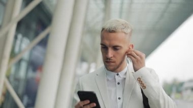 Genç çekici işadamı telefon kullanarak sokakta yürüyor. İş Merkezi etrafında yürüyüş kulaklık müzik dinlediği