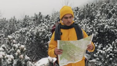 Dağlarda seyahat. Genç adam sarı kış giyim ormanda yürüyüş harita tutarak karla kaplı. Gezi, macera, tırmanma