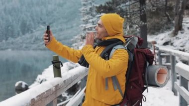 Genç yolcusu adam kış tatil görüntülü sohbet sahip. Onun arkadaş kış paylaşımı cep telefonu kamera webcam, sallayarak uzun yürüyüşe çıkan kimse macera tatil seyahat