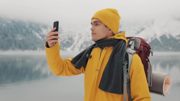 Hombre excursionista usando smartphone tomando una foto de la naturaleza invernal. El turista admira la naturaleza y hace fotos.Joven de pie sobre el fondo de hermosas montañas — Vídeos de Stock