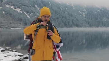 Güzel göl ve dağların kış zamanında. Amerikalı turist sarı kış giysileri giyen bayrak ile sıcak çay veya kahve dışında soğuk içme