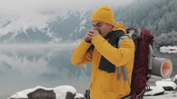 冬時間で美しい山々。ハイカーの男黄色の冬の服を着ては寒さの中の熱いお茶やコーヒーを外を飲んでいます。 — ストック動画