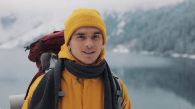 Kış giysileri içinde genç çekici bir adam portresi. Sarı kış giysileri giyen yürüyüş adam kamera ve gülümsüyor görünüyor. Güzel dağ ve göl karla kaplı arka plan
