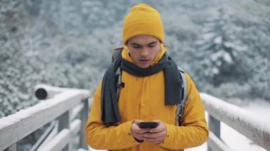 Genç turist karlı dağlarda bir köprü onun elinde bir akıllı telefon ile yürür. İletişim, sosyal ağlar, seyahat kavramı