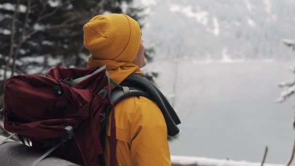 Egy izgatott srác sárga téli ruhában már egy hátizsák, a vállán. Túrázó felmászott a hegyre, és élvezi a kilátás a fák és egy enyhe köd, télen — Stock videók