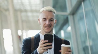 Genç çekici insan kahve tutarak ve telefon kullanarak sokakta yürüyor. İş Merkezi etrafında yürüyüş kulaklık müzik dinlediği