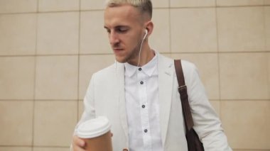 Çekici genç iş adamı ayakta ofis ve komik ritmine dans dışında smartphone, kulaklıktan müzik. Komik dans hamle kahve. Ağır çekim