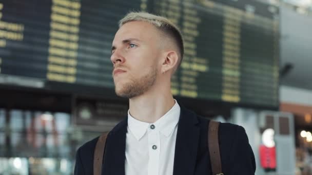 Jeune homme d'affaires attrayant attendant des amis près de l'écran du tableau des horaires à l'aéroport. Il agite la main, rencontre des amis — Video