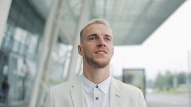 Bina ve kameraya bakarak ofisinin yürüyüş yakışıklı mutlu gülümseyen iş adamı portresi. Memnun ve mutlu görünen adam