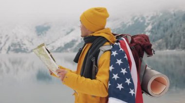 Dağlarda seyahat. Genç Amerikan uzun yürüyüşe çıkan kimse bir kağıt harita alanı kullanır. Yolunu arar. Macera ve seyahat hoşlanıyor. Bir arka plan kış dağlar ve güzel bir göl üzerinde