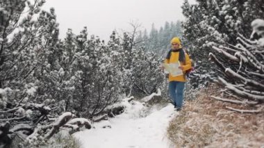 Dağlarda seyahat. Genç adam sarı kış giyim ormanda yürüyüş harita tutarak karla kaplı. Gezi, macera, tırmanma