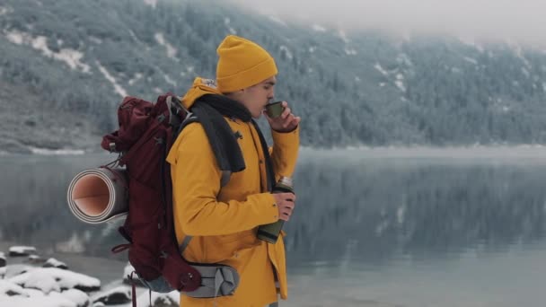 Schöne Berge im Winter. Wanderer in gelber Winterkleidung trinkt bei Kälte draußen heißen Tee oder Kaffee — Stockvideo