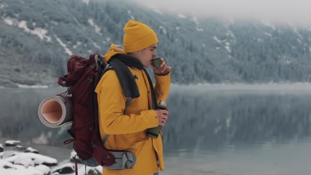 Beautiful mountains in winter time. Hiker man wearing yellow winter clothes is drinking hot tea or coffee outside in cold Stock Video