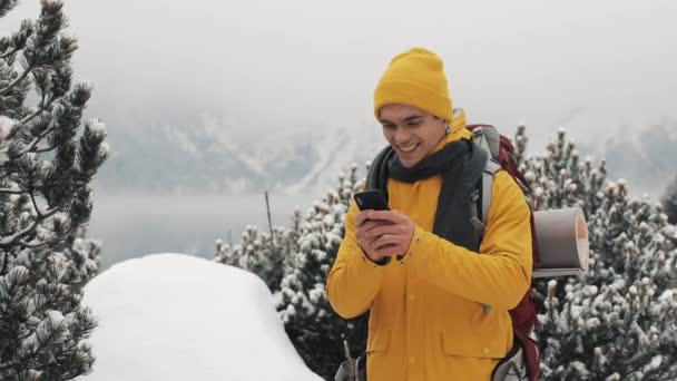 Junger Reisender mit Smartphone beim Winterwandern. schneebedeckte Berge Kap und See. Reise- und Kommunikationskonzept: Wanderer scrollen und tippen online per Handy — Stockvideo