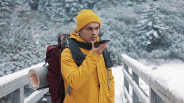 Onun elinde bir akıllı telefon ile karlı dağlarda bir köprüde duran genç bir turist. Konuşmayı ile sesli mesaj yazmak dışında Smartphone fiyatı