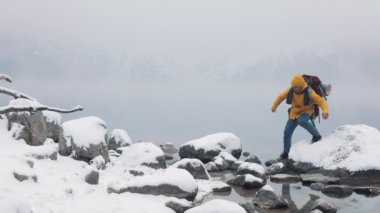 Dağlarda seyahat. Sarı kış giyim dağ Gölü yakınındaki taş üzerinde yürüyen bir genç adam. Kış saati tırmanma gezi, macera,