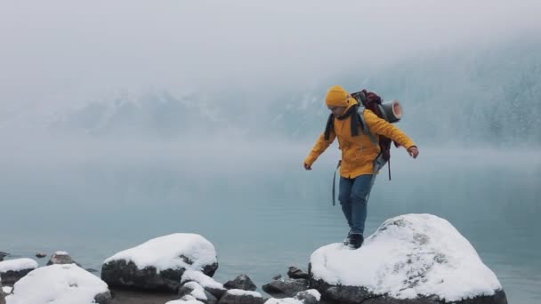 在山里旅行 美国徒步者穿着黄色冬衣 在山湖附近的石头上行走 冬季旅行 — 图库视频影像