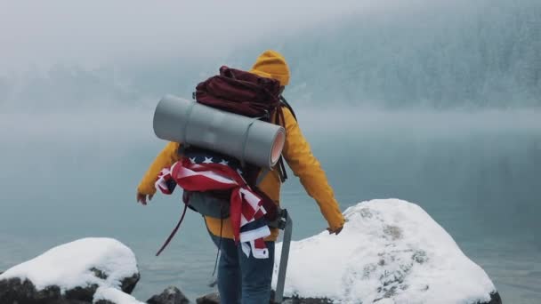 Gli escursionisti americani indossano indumenti invernali gialli camminando sulle pietre vicino al lago di montagna e alzando le mani sul concetto di vincitore della cima della montagna. Escursioni escursionismo alpinismo invernale trekking — Video Stock