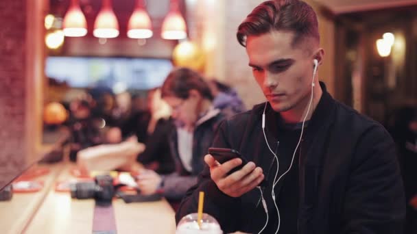 Ung man lyssna på musik på smartphone i café på natten — Stockvideo