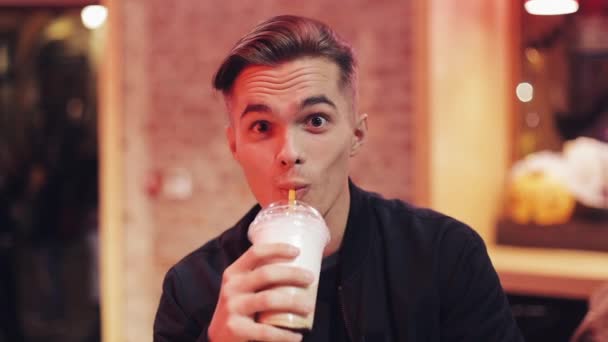Красивый молодой человек пьет молочный коктейль и смотрит в камеру. Он сидит за баром в ночном кафе. Медленное движение — стоковое видео