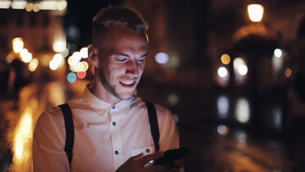 Giovane uomo attraente utilizzando smartphone a piedi sulla strada della città di notte. Comunicazione, viaggi, turismo, incontri, business concept — Video Stock