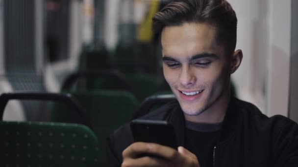 Joven feliz usando el teléfono inteligente mientras viaja en tranvía, disparo steadicam. Movimiento lento — Vídeo de stock