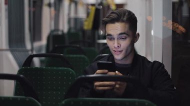 Tramvay, atış steadicam sürme sırasında akıllı telefon kullanan mutlu genç adam. Ağır çekim