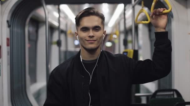 Hombre guapo con auriculares mirando a la cámara en el tranvía y sonriendo, steadycam disparo. Primer plano — Vídeos de Stock