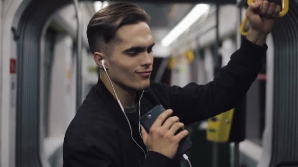 Retrato de hombres guapos en auriculares escuchando música y bailando divertido en transporte público. Él sostiene la barandilla — Vídeos de Stock