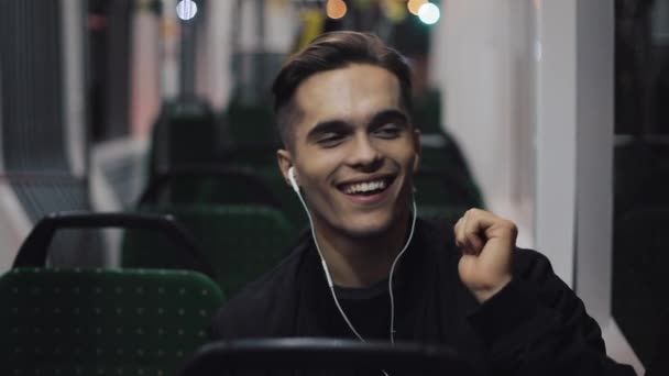 Hombres guapos en auriculares escuchando música y bailes divertidos sentados en el transporte público. Él sostiene la barandilla — Vídeo de stock