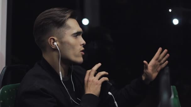 Hombres guapos en auriculares escuchando música y bailes divertidos sentados en el transporte público. Él sostiene la barandilla — Vídeos de Stock