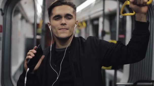 在公共交通工具上听音乐和有趣舞蹈的英俊男子的肖像 他拿着扶手 — 图库视频影像