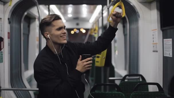 音楽や公共交通機関で面白い踊りを聴くヘッドフォンでハンサムな男性の肖像画。彼は手すりを保持します。 — ストック動画