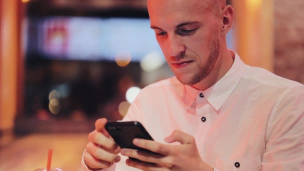 Młody mężczyzna atrakcyjny smartfona na wieczór. On siedzi w barze lub restauracji w pobliżu neon signage. Komunikacji, reszta, na czacie, koncepcja podróży. Z bliska — Wideo stockowe