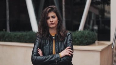 Ofis onun önünde çapraz elle kameraya gülümseyen Binası yakınında duran genç çekici kadın portre vurdu. O bir sıcak sarı kazak ve sonbahar deri ceket giymiş