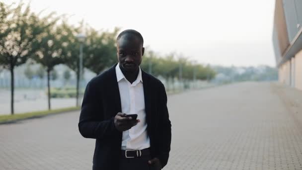 Ritratto di uomo d'affari afroamericano di successo con smartphone in piedi vicino all'edificio degli uffici e guardando nella fotocamera. Concetto: nuova attività, viaggiare per il mondo — Video Stock