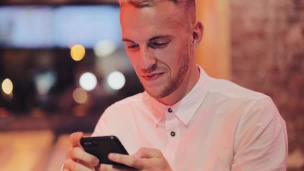 Młody Mężczyzna Atrakcyjny Smartfona Wieczór Siedzi Barze Lub Restauracji Pobliżu — Wideo stockowe
