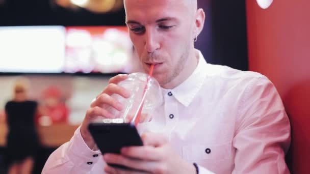 Akşam saatlerinde Smartphone kullanan genç çekici adam. O, bir bar veya restoran neon tabela yakın oturan ve kokteyl içme. İletişim, dinlenme, sohbet, seyahat kavramı. Yakın çekim — Stok video