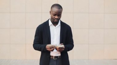 Office merkezine yakın para ayakta sayma takım elbiseli Afrikalı-Amerikalı işadamı portresi. O onun başarılı kazanmak dolar bir çok ile kutluyor ve kameraya bakıyor