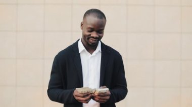 Office merkezine yakın para ayakta sayma takım elbiseli Afrikalı-Amerikalı işadamı portresi. O onun başarılı kazanmak dolar bir çok ile kutluyor ve kameraya bakıyor.