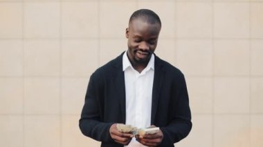 Office merkezine yakın para ayakta sayma takım elbiseli Afrikalı-Amerikalı işadamı portresi. O onun başarılı kazanmak dolar bir çok ile kutluyor ve kameraya bakıyor