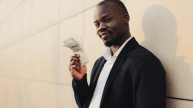 Büyük miktarda para onun elinde tutan mutlu Afrika kökenli Amerikalı iş adamı. Ofis merkezi veya banka yakınlarında sokakta duruyor. İş tarzı, kazanç, para, başarı, kariyer