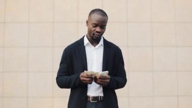Office merkezine yakın para ayakta sayma takım elbiseli Afrikalı-Amerikalı işadamı portresi. O onun başarılı kazanmak dolar bir çok ile kutluyor ve kameraya bakıyor