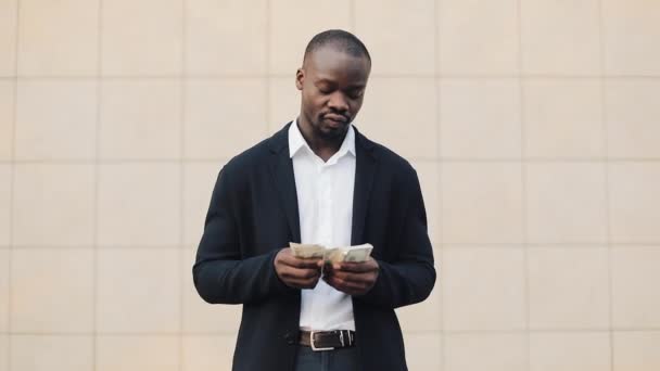 Portret van Afro-Amerikaanse zakenman in pak geld staande in de buurt van office centrum tellen. Hij viert zijn succesvolle win met veel dollars en op zoek naar de camera — Stockvideo