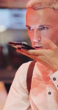 Adam ses tanıma ile neon bar işareti yanında oturan smartphone. emir bekliyoruz, turistik kullanmak mesaj ses yardımcı Bulucu