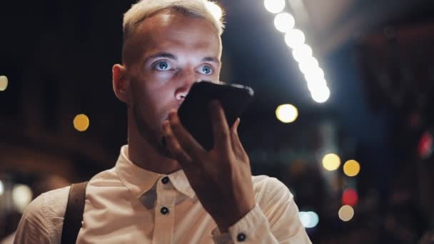 Un uomo sorridente che fa videochiamate su smartphone a Night City. Bel giovanotto che usa lo smartphone di notte. Concetto di mobilità — Video Stock