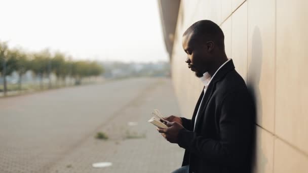 Steht der junge erfolgreiche afrikanisch-amerikanische Geschäftsmann auf der Straße und zählt das Geld. schaut er in die Kamera. Erfolgreiche Geschäfte, Gewinne, Lotterie, Konzept des einfachen Geldes — Stockvideo