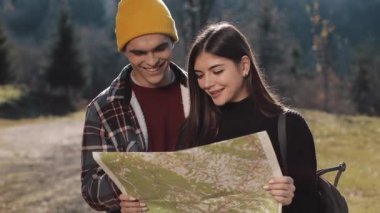 Mutlu çift ayakta dağlarda gülümseyen genç. Onlar onların yürüyüş zevk almak. Turistik harita üzerinde seyir. Yön bulmaya çalışıyorum. Ağır çekim